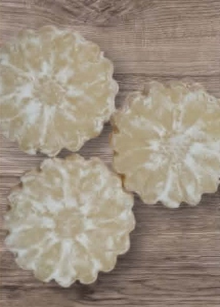Three round, white floral-patterned cookies on a wooden surface