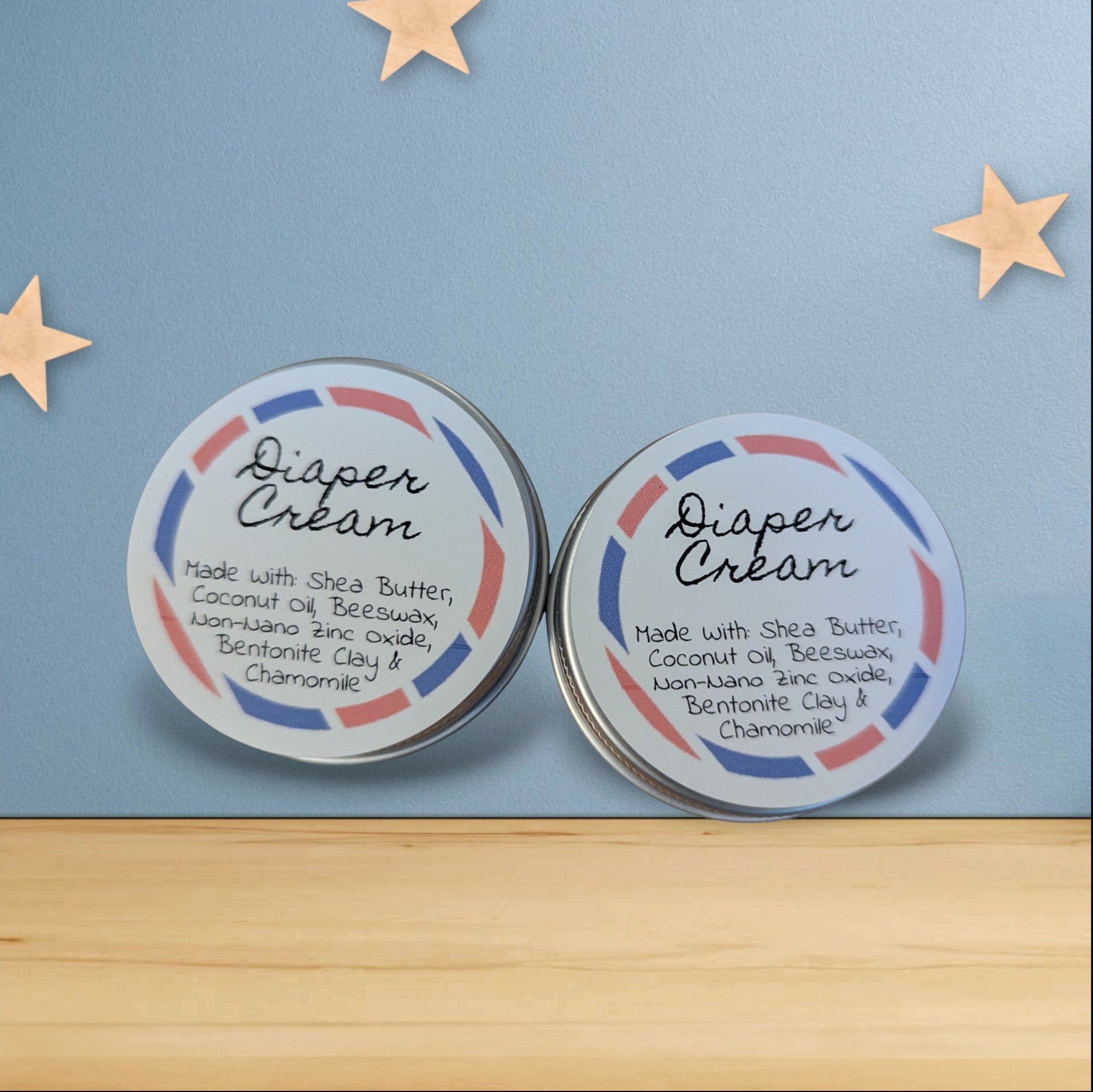 Two tins of diaper cream on a wooden surface with a blue background and gold stars.