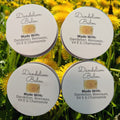 Four containers of Dandelion Balm with dandelions in the background