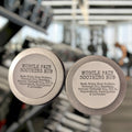 Two containers of Muscle Pain Soothing Rub with a gym background
