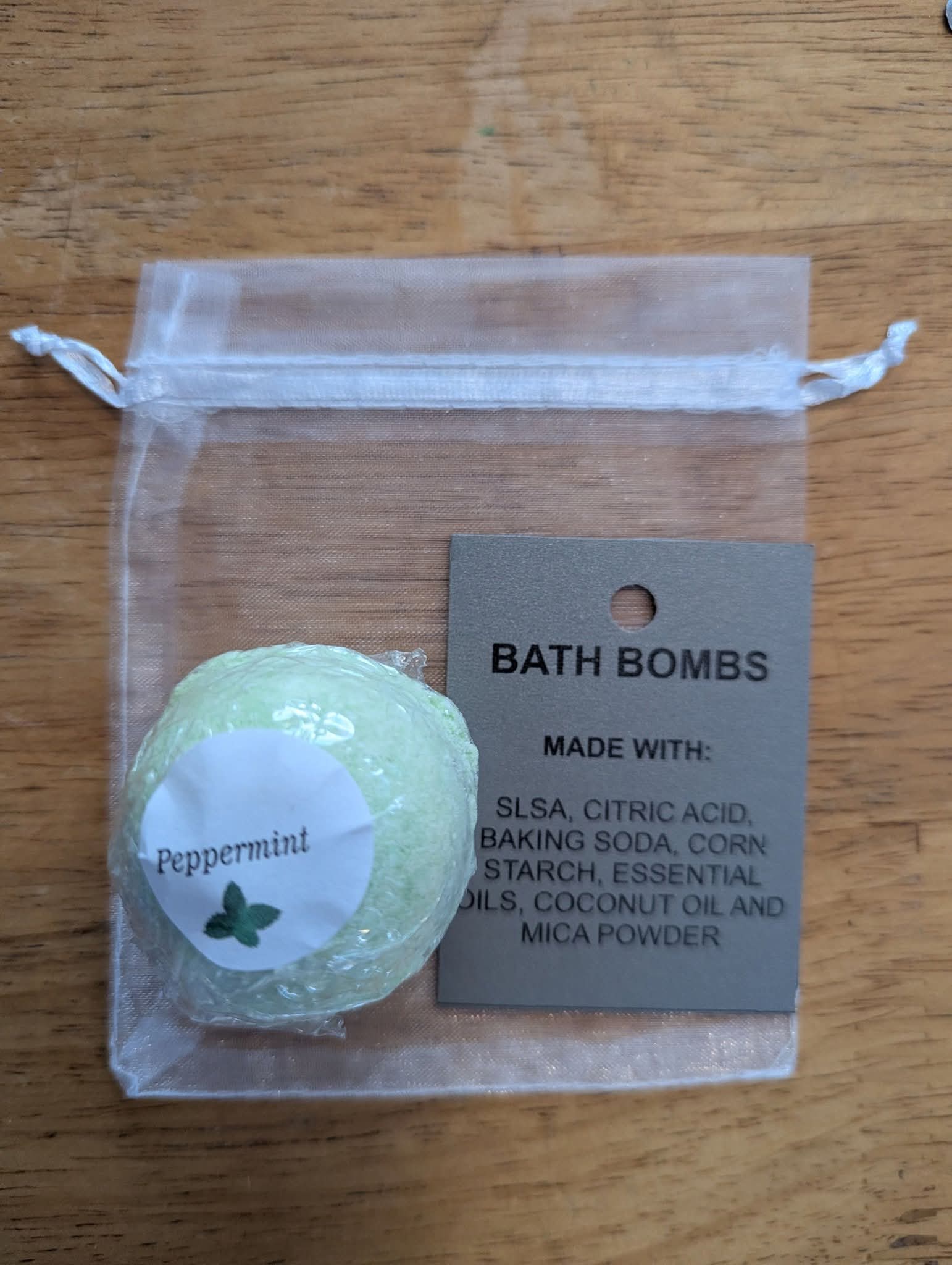 Green bath bomb in a clear drawstring bag with a label on a wooden surface